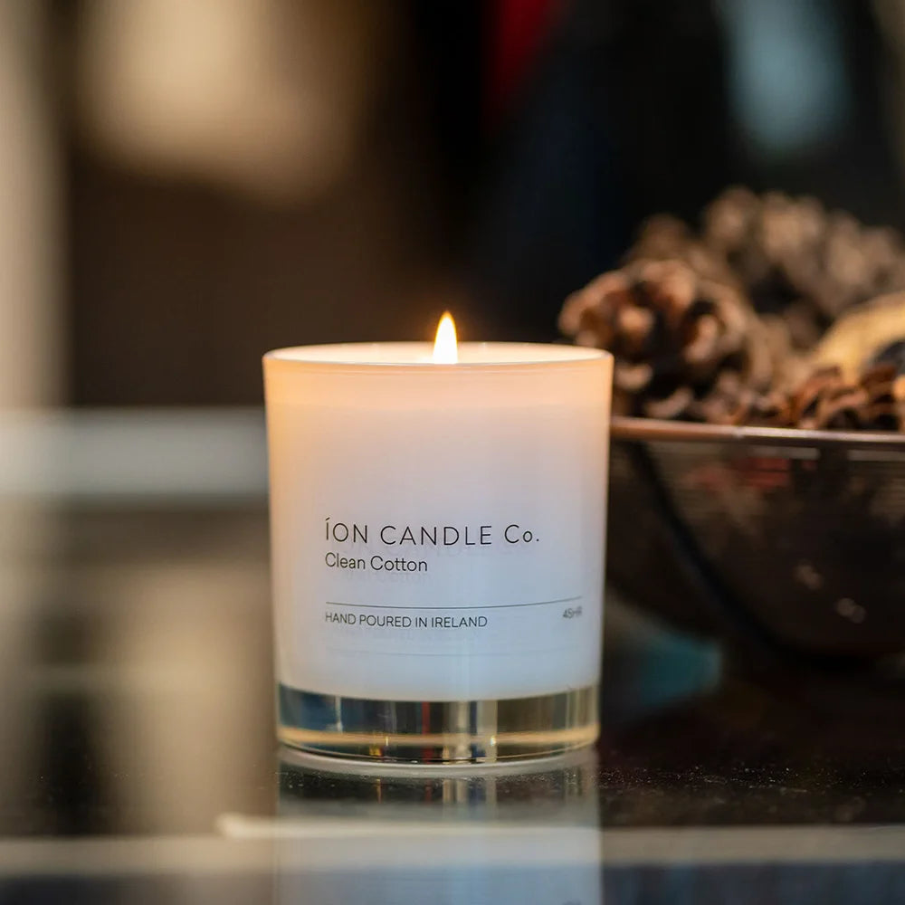 Ion Candle Co. - Clean Cotton Luxury Scented Candle. The candle is lit and placed on a dark shiny countertop
