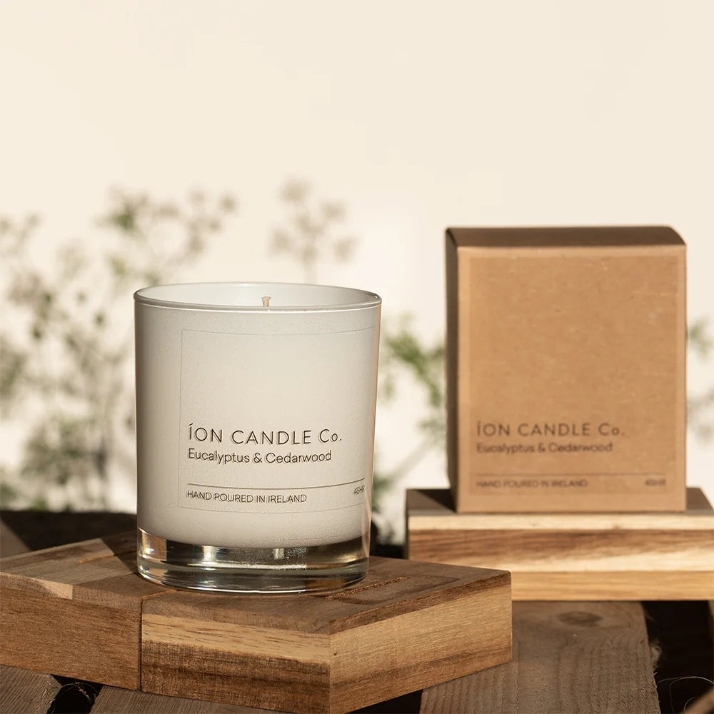 Ion Candle Co. - luxury scented eucalyptus & cedarwood candle placed on a wooden block against a floral background