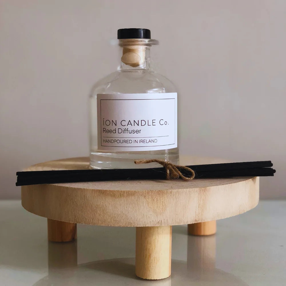 Ion Candle Co. - Scented Reed Diffuser bottle on a small wooden stand against a beige background