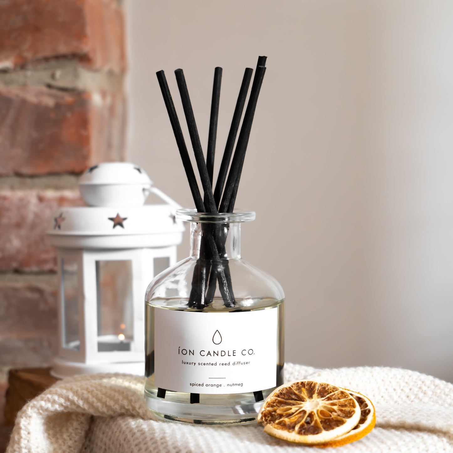Diffuser bottle with black sticks and dried orange on a textured surface with a neutral background