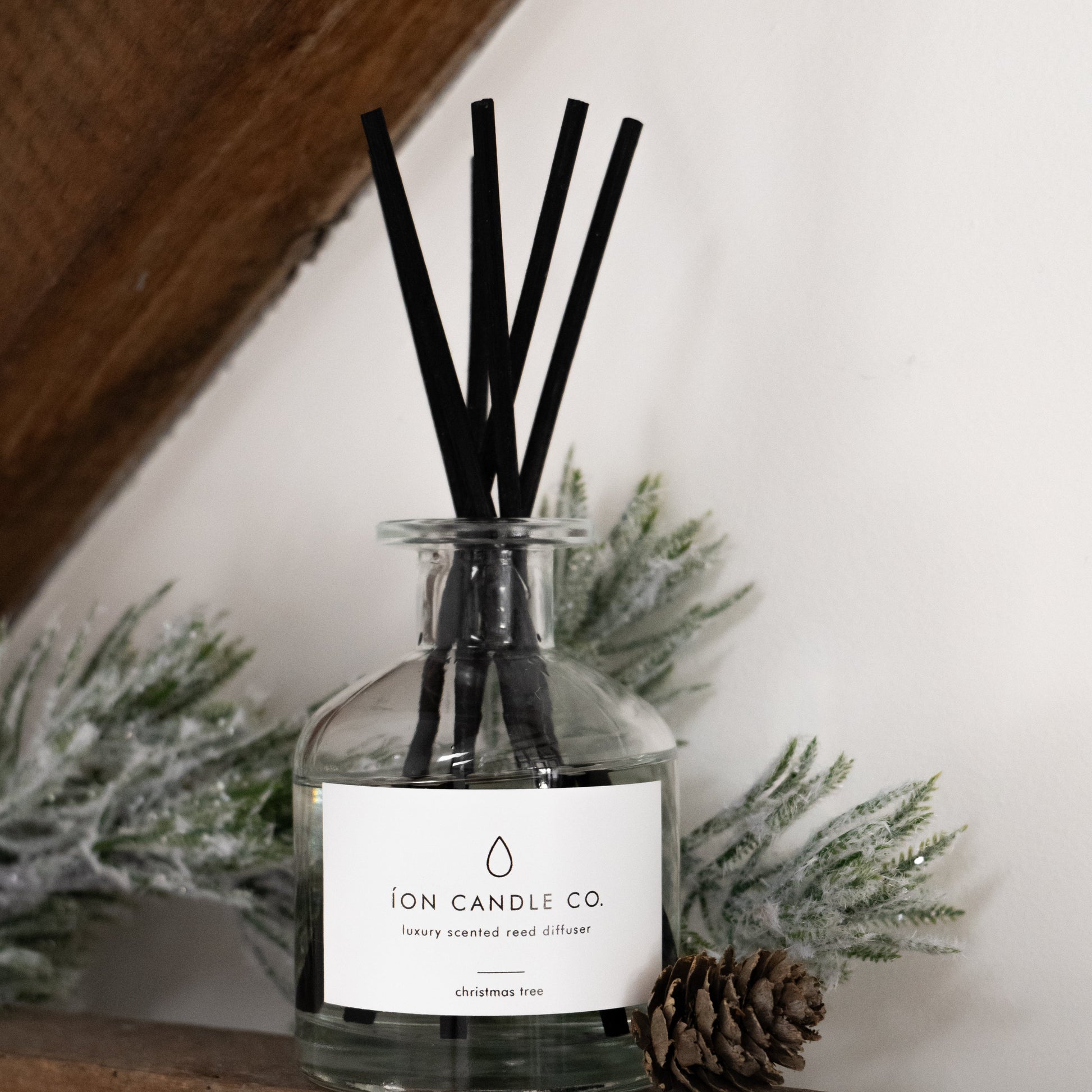 Reed diffuser with black sticks in a clear bottle on a wooden surface with decorative elements.