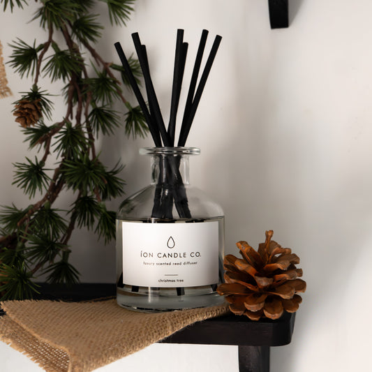 Diffuser with black sticks on a small black stand with a pine cone and branches in the background