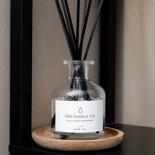 Diffuser with black reeds on a wooden tray on a shelf, featuring Ion Candle Co branding.