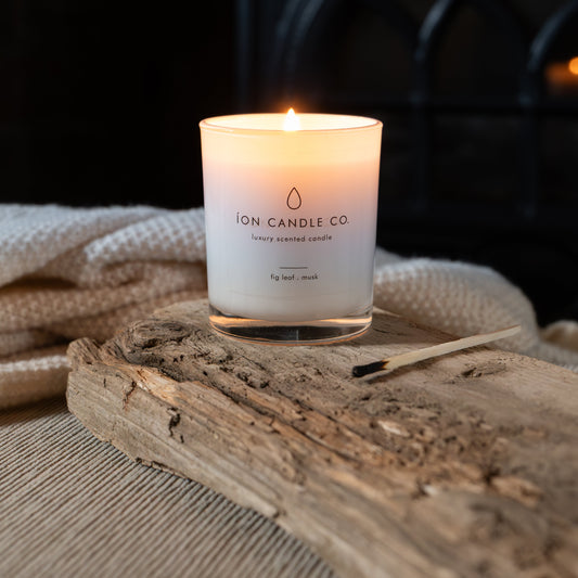Fig leaf and musk candle in white jar placed on driftwood lighting qith fire backdrop 