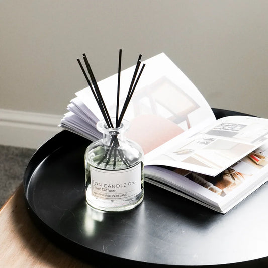 Ion Candle Co. - Jasmine & Green Vetiver Luxury Irish Reed Diffuser bottle sat on a black serving tray next to an open book