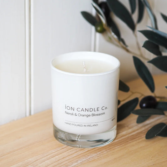 Ion Candle Co. - Neroli & Orange blossom luxury scented candle, placed on a pine wood shelf next some foliage