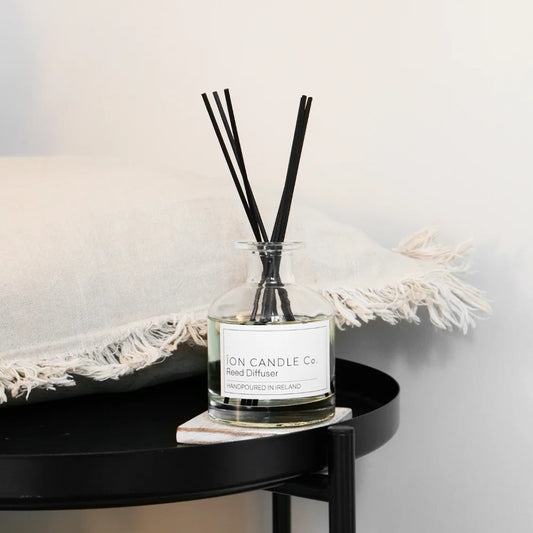 Ion Candle Co. - Rocksalt & Driftwood Reed Diffuser bottle on a circular black coffee table with a white cushion next to it
