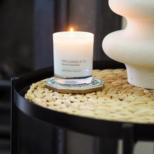 Ion Candle Co. - Luxury scented spiced tonka bean candle, placed on a wicker straw coffee table next to a vase