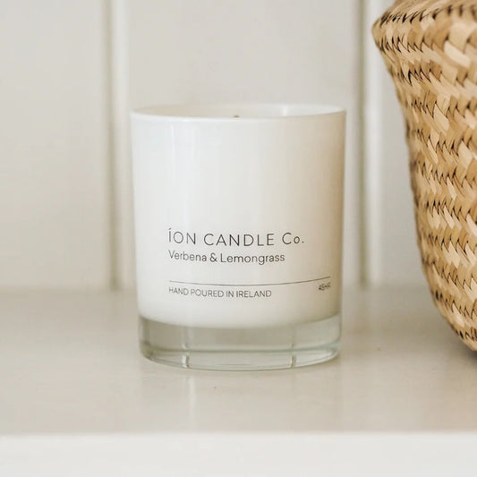 Ion Candle Co. - Luxury scented verbena & lemongrass candle placed on a white shelf next to a wicker straw basket