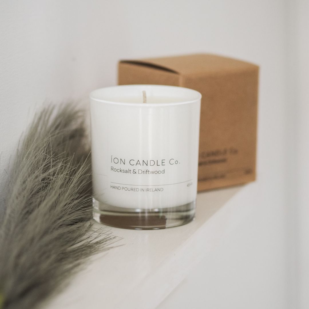 Ion Candle Co. - luxury scented rocksalt & driftwood candle, placed on a shelf next to a green feather