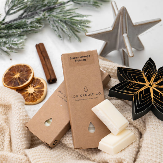 Two boxes of 'ION CANDLE CO' candles on a textured surface with decorative elements like cinnamon sticks and dried oranges.