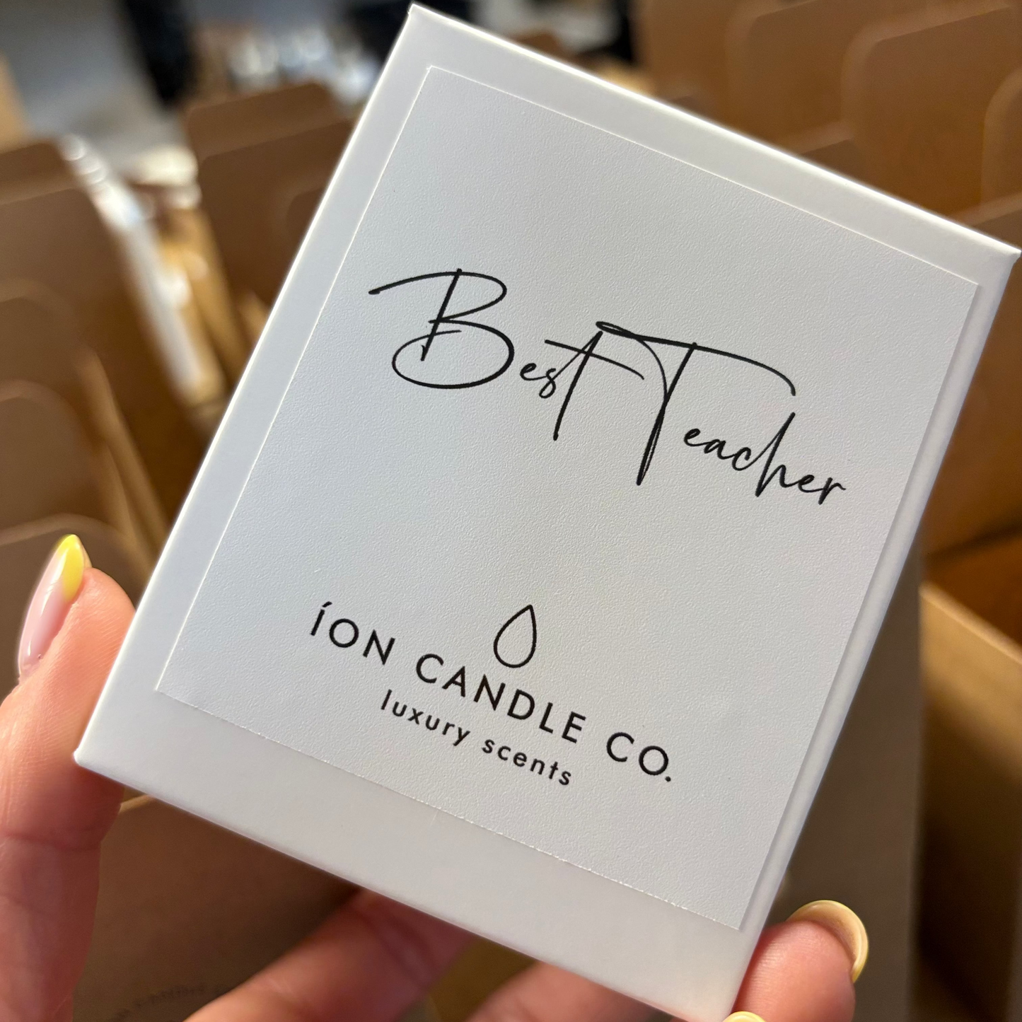 Hand holding a candle packaging labeled 'Best Teacher' by Ion Candle Co.