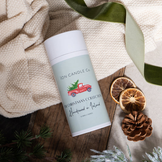 Candle on a wooden surface with decorative elements and a Christmas tree design on the label.