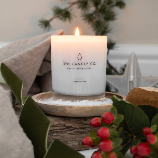 Lit candle with 'ION CANDLE CO' branding on a decorative surface with greenery and berries.