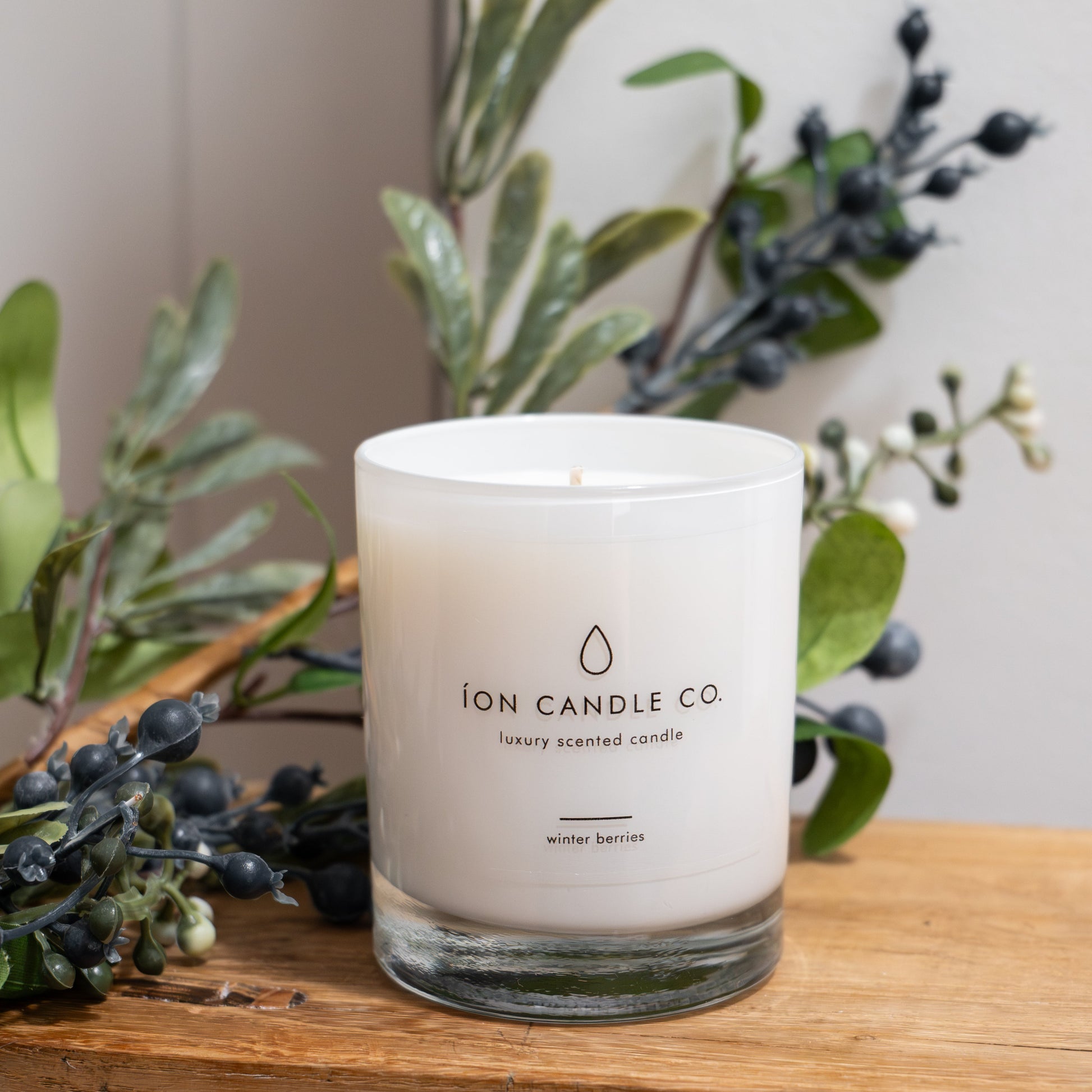 White candle with 'ION CANDLE CO' branding on a wooden surface with greenery in the background