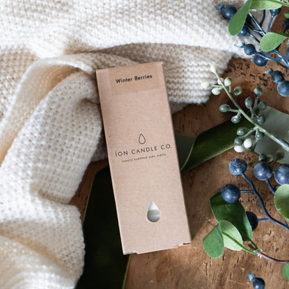 ION Candle Co. packaging on a wooden surface with a white blanket and greenery