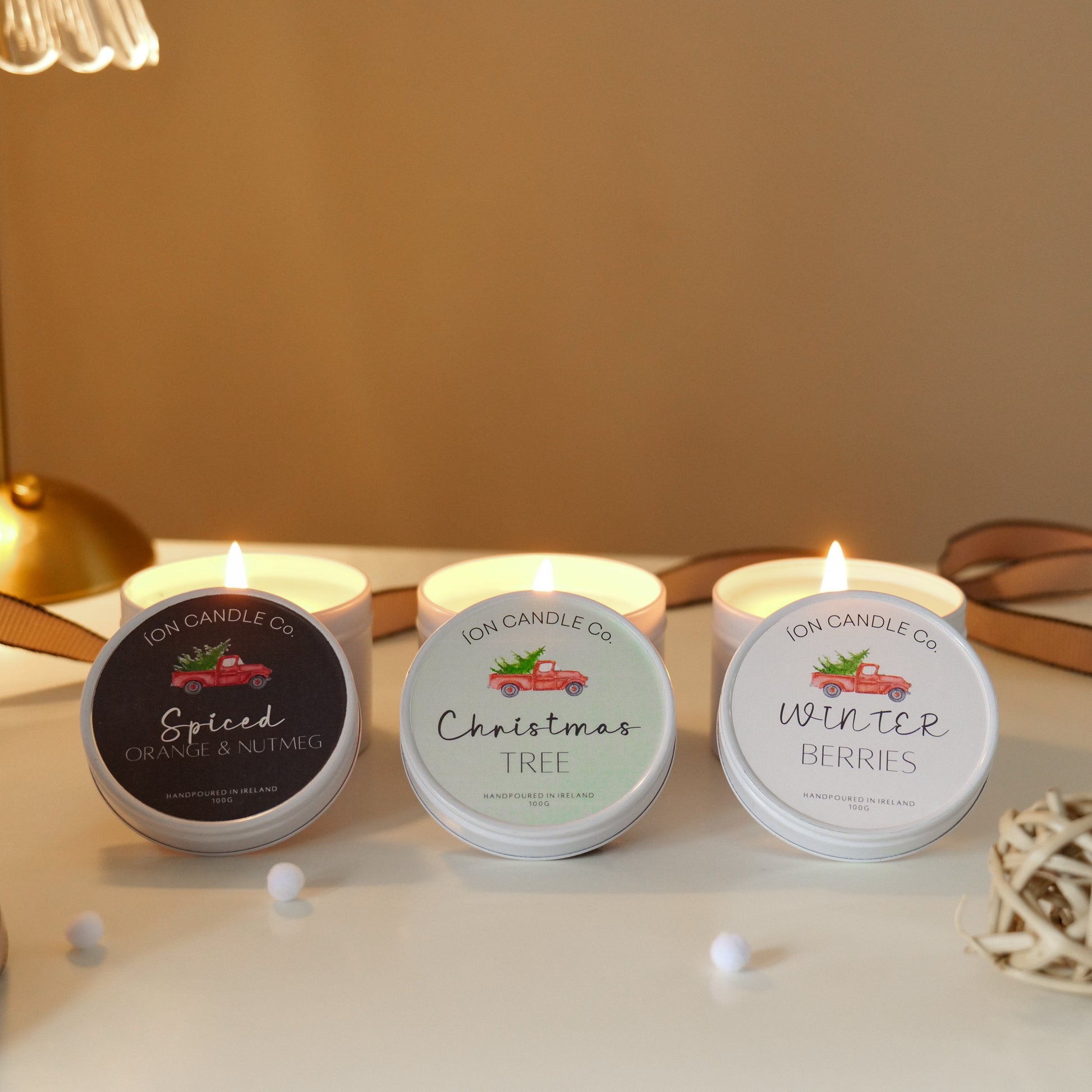 Three scented candles labeled 'Spiced Apple', 'Christmas Tree', and 'Winter Berries' on a table with decorative items.