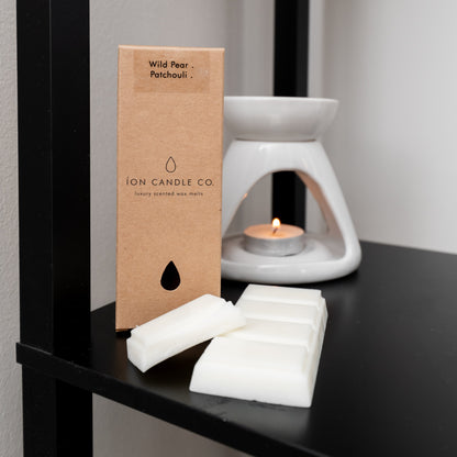 white wax burner with wax melt in kraft packaging and bars on a black surface