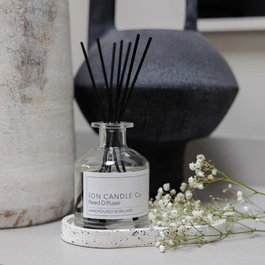 Styled image of Bergamot & amber reed diffuser with white flower and black vase 