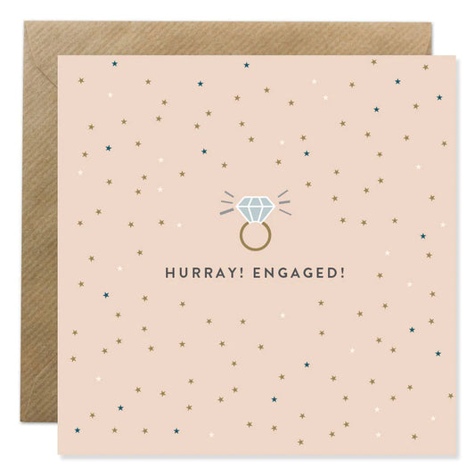 Ion Candle Co. - Engagement Greeting Card. The card is blush pink with various coloured dots scattered around text which is in the centre and reads 'Hurray! Engaged!'  Above the text is an image of a sparkling diamond ring